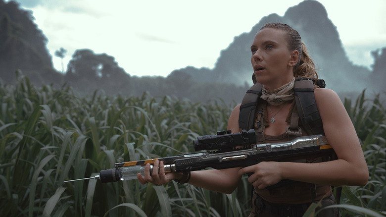 Zora Bennett marchant avec un gros pistolet à aiguille à travers de hautes herbes