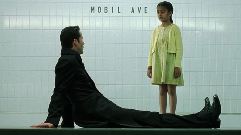 Neo parle à une petite fille dans une gare en 