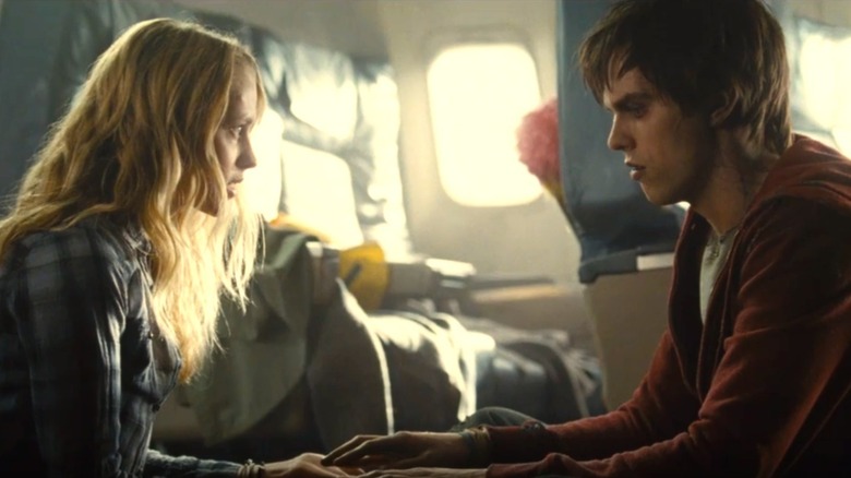 Julie et R sont assis en face de l'autre, touchant les mains