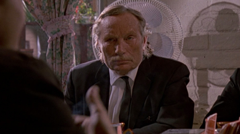 M. Blue assis à une table dans un costume dans les chiens de réservoir (1992)