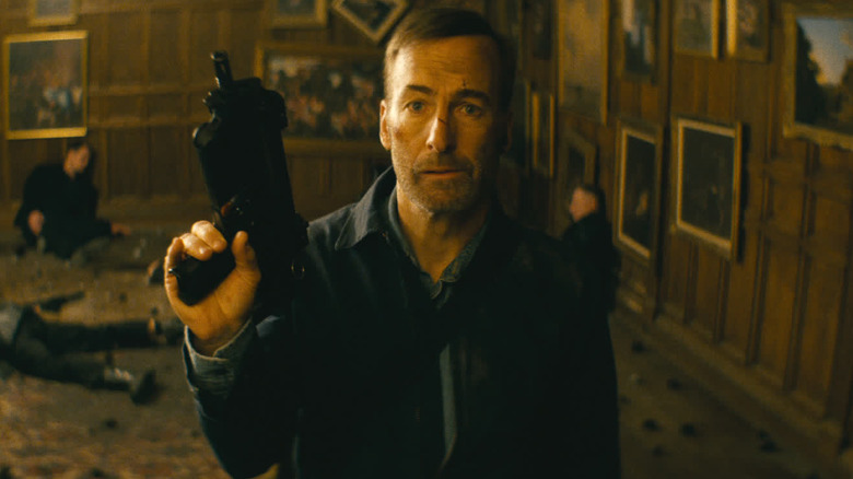 Hutch tenant un pistolet avec des corps derrière lui 