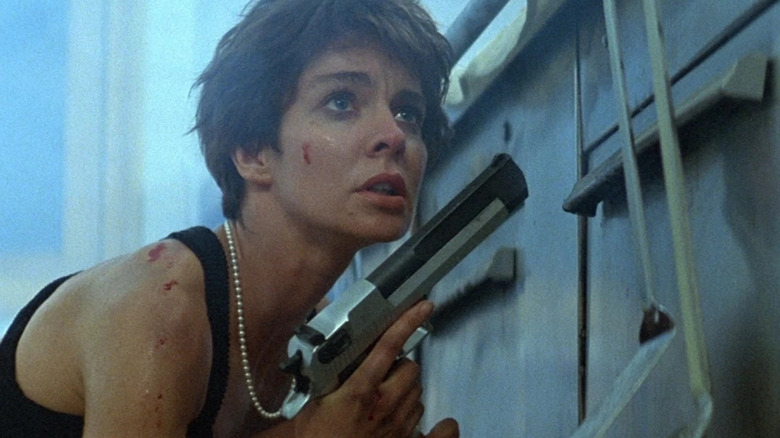 Nikita se cache derrière une benne à ordures avec un pistolet à La Femme Nikita