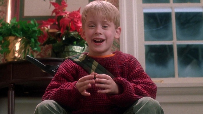 Kevin est assis avec son pistolet BB et sourit dans Home Alone (1990)