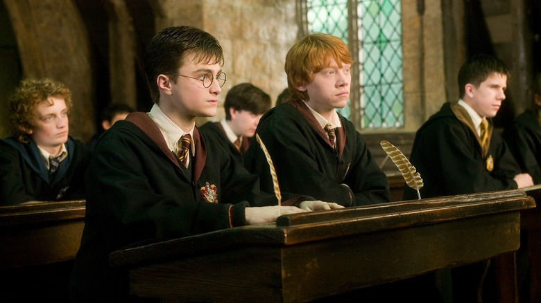 Harry et Ron assis ensemble en classe devant un bureau en bois sombre avec des plumes