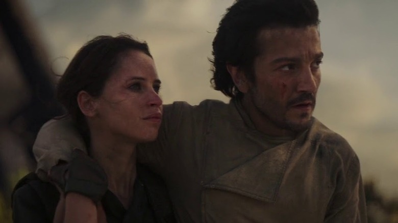 Cassian Andor tient son bras sur Jyn Erso, à la fois meurtri et sale alors qu'ils regardent l'horizon dans 