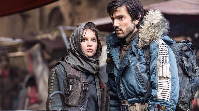 Jyn Erso portant une capuche sombre et Cassian Andor, vêtue d'une parka bleue, se tiennent dans un bazar du désert à 