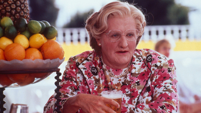 Mme Doubtfire assise dans un bar extérieur, buvant de la bière à côté d'un bol élaboré d'agrumes