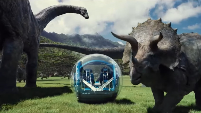 Un véhicule de tourisme passe devant un brontosaure et un tricératops dans Jurassic World