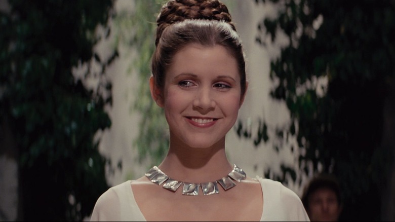 La princesse Leia sourit dans une robe blanche avec ses cheveux relevés. 