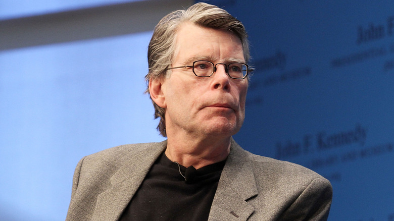 Stephen King avec une veste de costume grise et une chemise noire