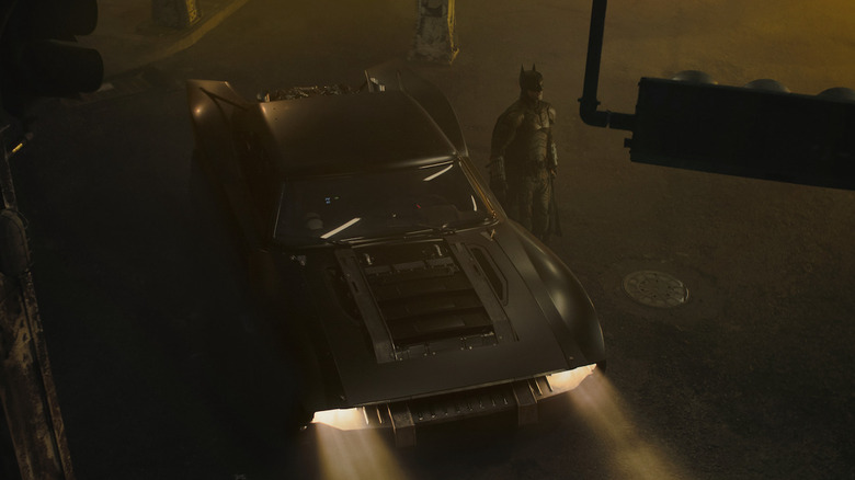 Batman à côté de la Batmobile à Gotham City la nuit