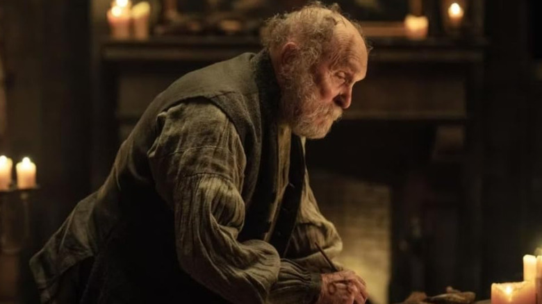 Jean-Pepe se penche pour écrire quelque chose dans L'Œil bleu pâle (2022)