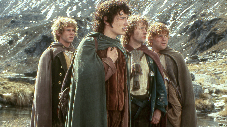 Joyeux, Frodon, Pippin et Sam debout dans un paysage montagneux