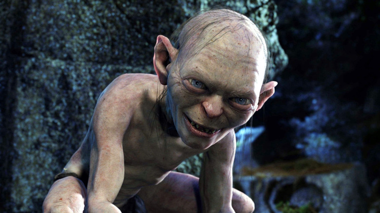 Gollum souriant et accroupi près d'un mur de pierre