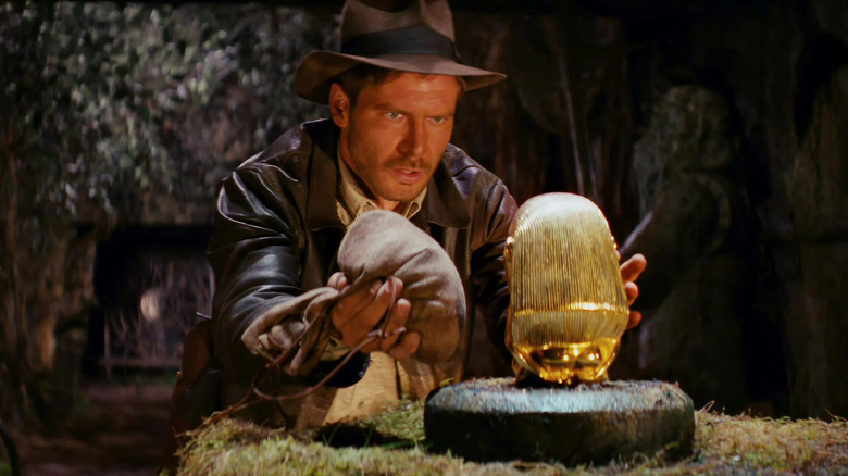 Indiana Jones tient un sac tout en cherchant une statue en or dans Les Aventuriers de l'arche perdue (1981)