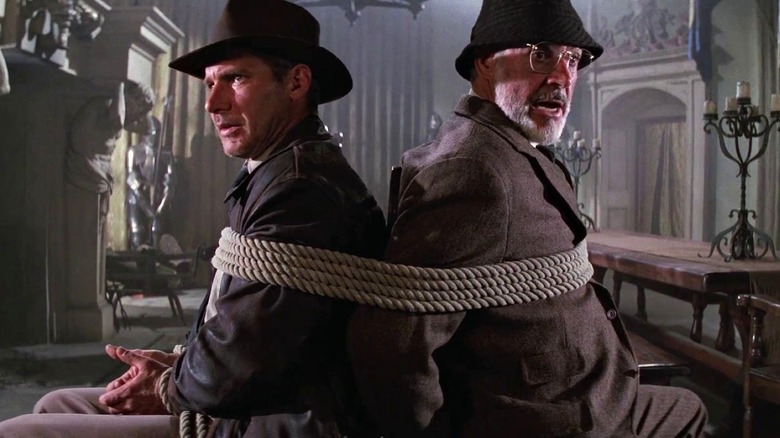 Indiana et Henry Jones sont assis l'un derrière l'autre alors qu'ils sont attachés dans Indiana Jones et la Dernière Croisade (1989)