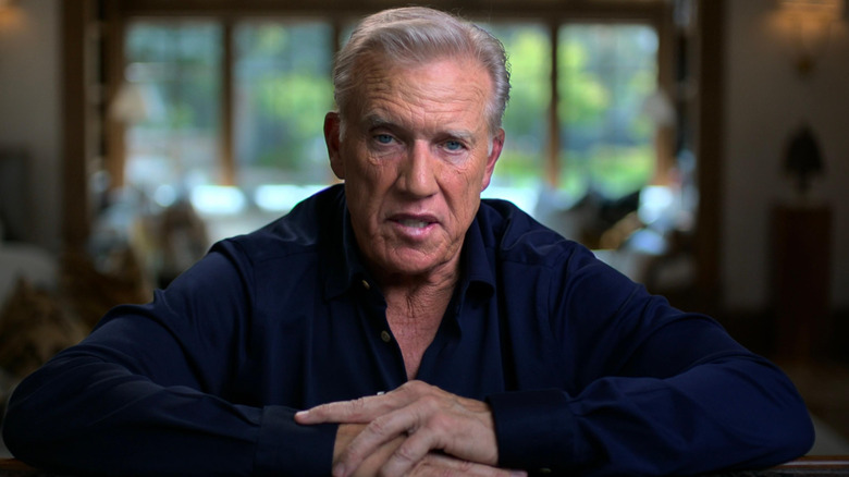 John Elway en chemise bleue parlant à la caméra dans Elway (2025)