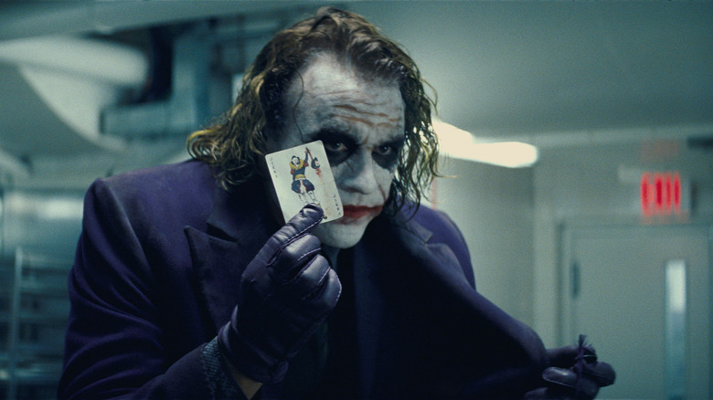 Le Joker tient une carte à jouer Joker tout en portant un costume violet 