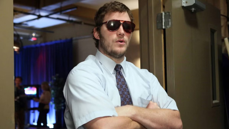 Andy Dwyer croise les bras tout en portant de grandes lunettes de soleil marron 