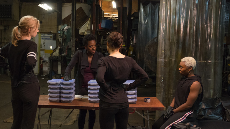 Quatre femmes se tiennent autour d'une table avec des piles d'objets devant elles, toutes vêtues de noir, dans 