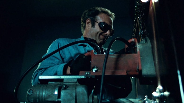Un homme en combinaison tient un gros matériel mécanique tout en portant des lunettes 