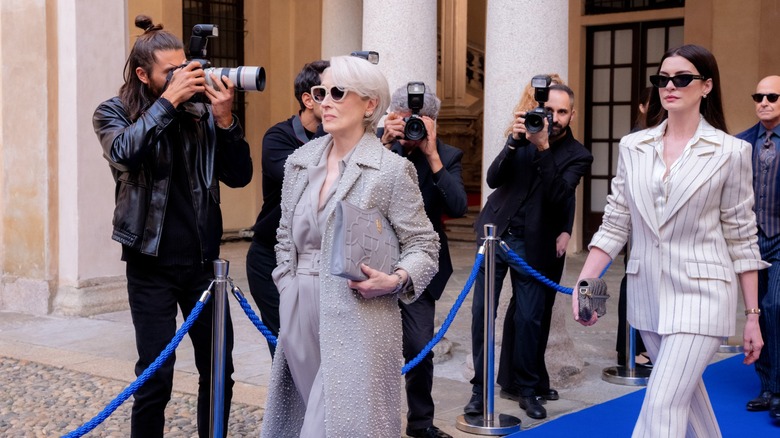 Miranda et Andy sortant d'un immeuble à Milan et se faisant photographier dans Le Diable s'habille en Prada 2