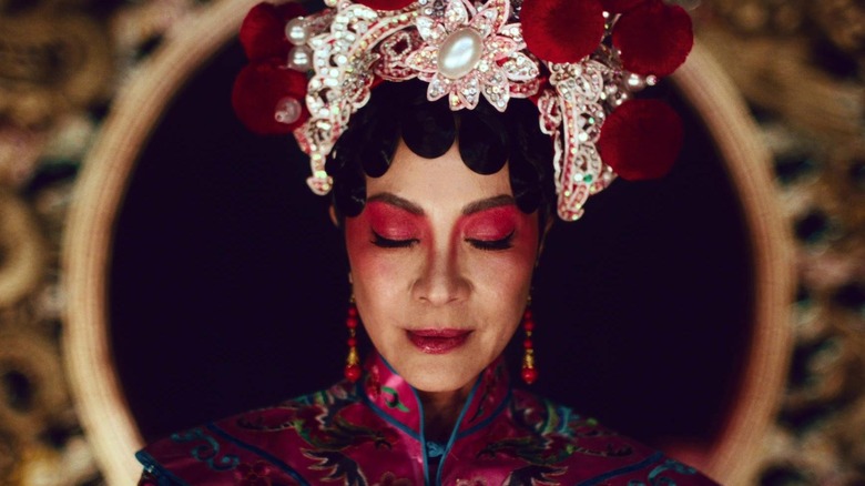 L'un des personnages alternatifs d'Evelyn portant des parures ornées et un maquillage dramatique, les yeux fermés.