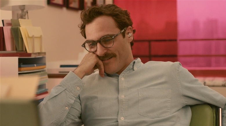 Theodore Twombly souriant à son bureau avec des écouteurs sur elle