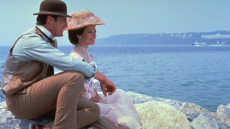 Richard et Elise assis sur des rochers au bord d'un lac dans Somewhere in Time