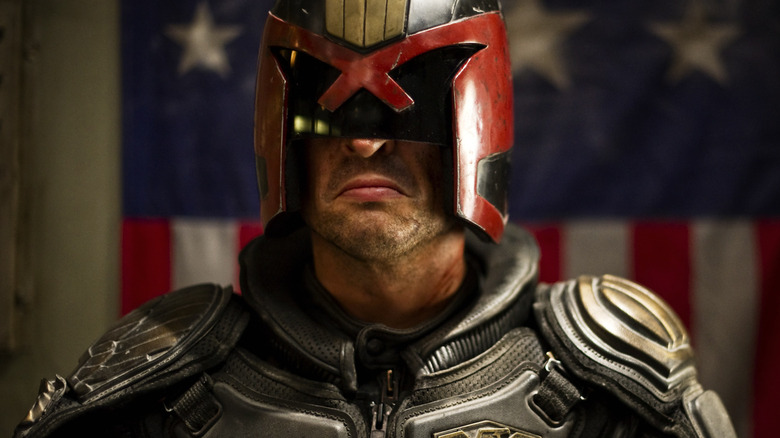 Le juge Dredd renfrogné devant un drapeau rouge, blanc et bleu dans Dredd (2012)