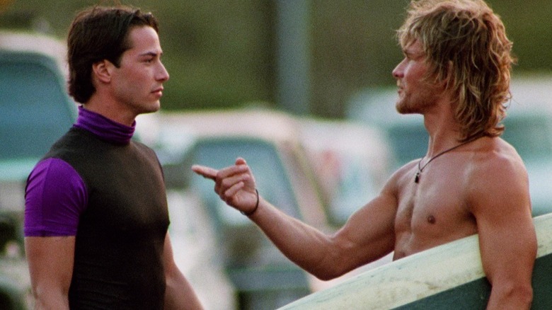 Bodhi tenant sa planche de surf et montrant Johnny Utah dans Point Break
