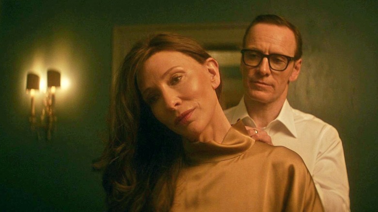 George attache un collier autour du cou de Kathryn dans un couloir faiblement éclairé. 