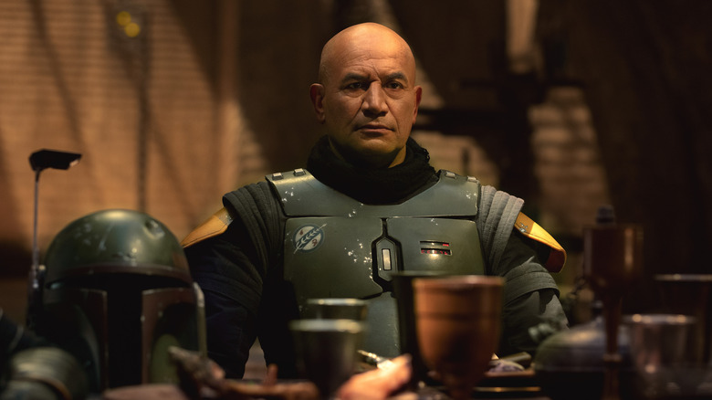 Boba Fett assis à une table, armure mais casque retiré, dans Le Livre de Boba Fett (2021)
