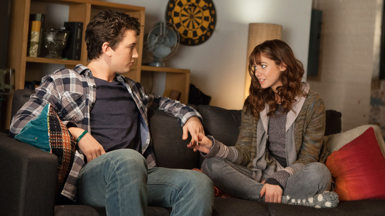 Alex et Megan assis sur le canapé, se tenant la main dans Two Night Stand