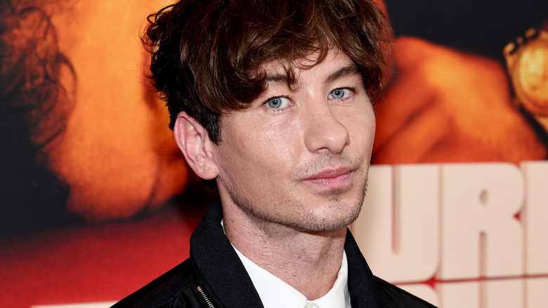 Gros plan de l'acteur Barry Keoghan posant devant une affiche de film et des lettres majuscules blanches lors d'une première sur un tapis.