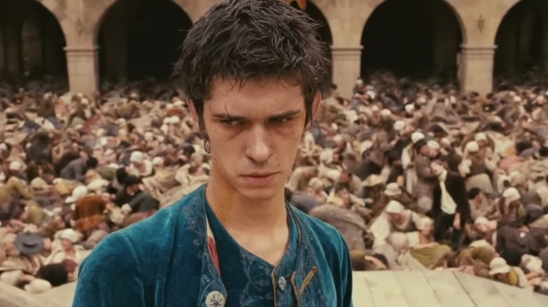Jean-Baptiste Grenouille debout sur une estrade de la place de la ville, alors que les gens se tordent par terre autour de lui, en 