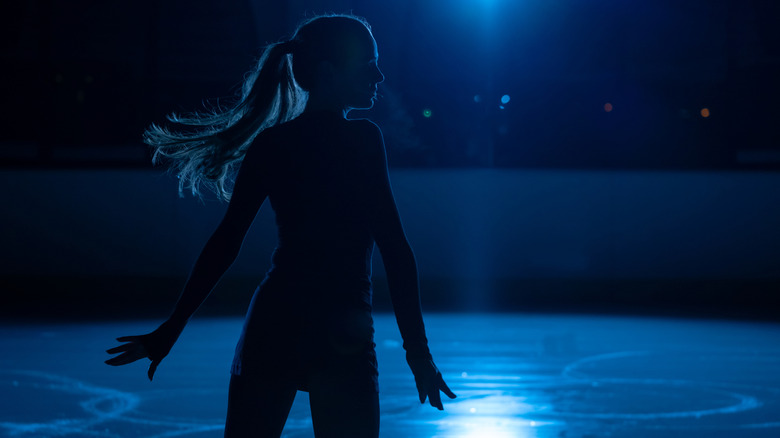 Silhouette d'une jeune femme patinant sur glace dans le noir
