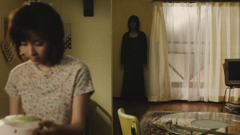 Une silhouette sombre se tient contre un mur tandis qu'une femme est assise, inconsciente, au premier plan. 