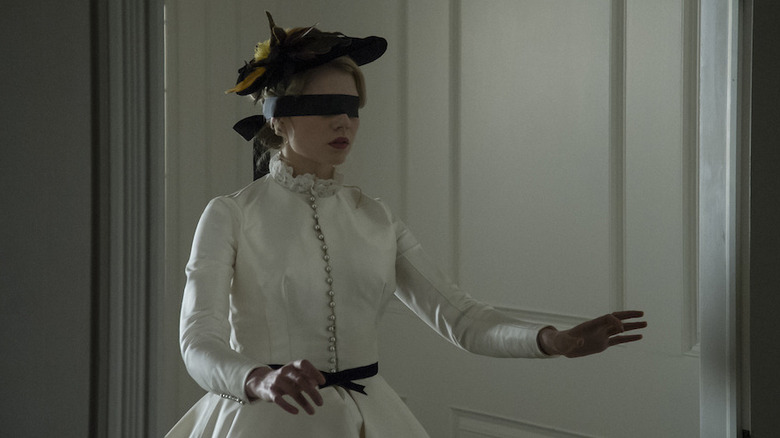 Lucy, les yeux bandés, marche avec les mains tendues devant elle. 