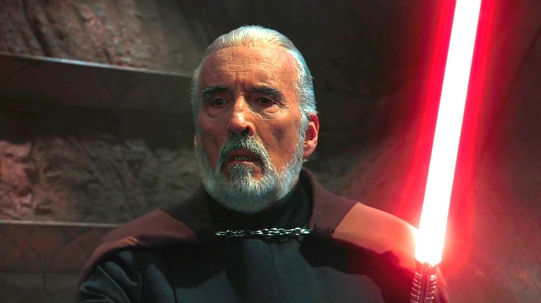 Le comte Dooku renfrogné avec son sabre laser rouge allumé face à Obi-Wan et Anakin dans L'Attaque des Clones (2002)