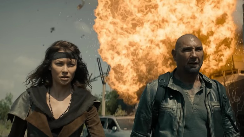 Drea et Jake marchent vers la caméra, loin d'une explosion massive, dans Afterburn
