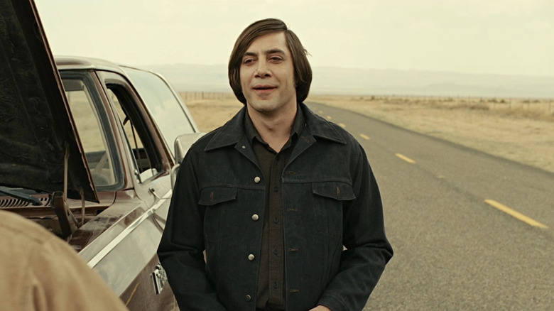Anton Chigurh se tient à côté d'une voiture avec le capot relevé dans No Country for Old Men (2007)