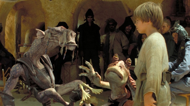 Sebulba, Jar Jar et le jeune Anakin discutent dehors.