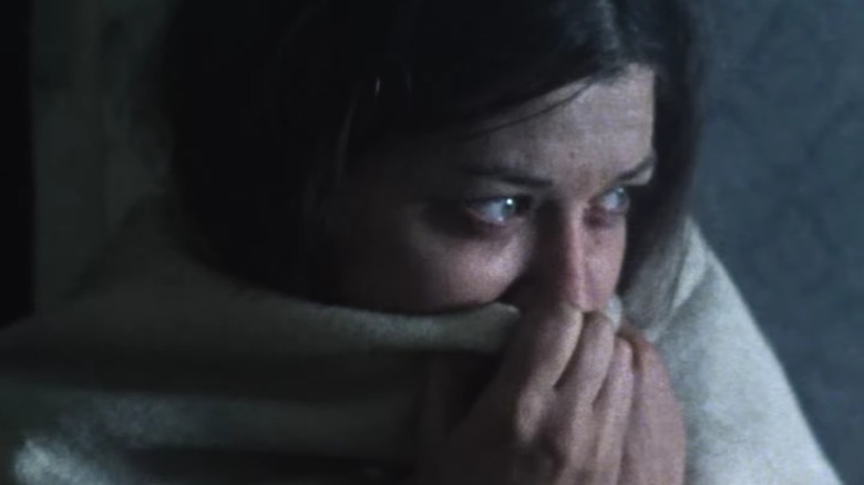 Une figurante dans Threads tire une couverture autour de son visage, ses yeux remplis de larmes sont visibles par-dessus.