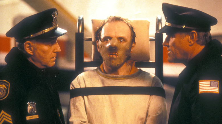 Hannibal Lecter en camisole de force et masque, flanqué de flics