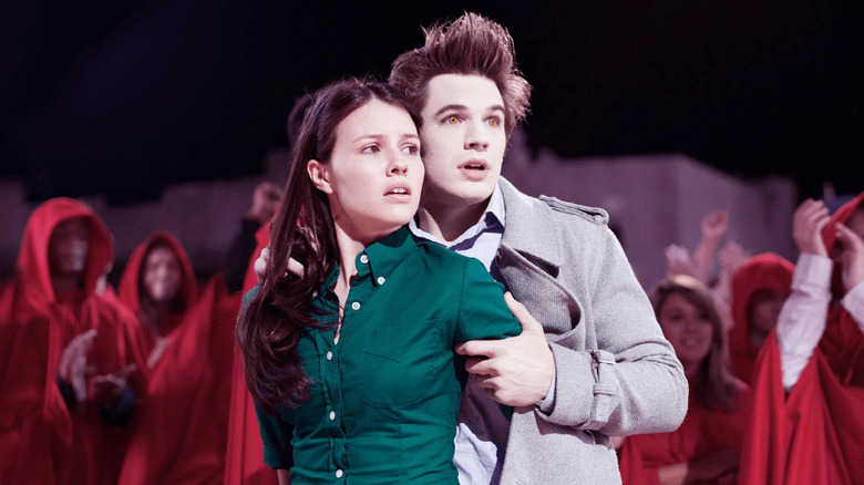 Edward tient Bella de manière protectrice tandis que des silhouettes en robe se profilent derrière eux.