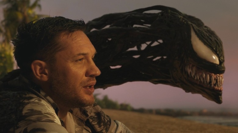 Eddie Brock assis à côté de Venom sur une plage de 