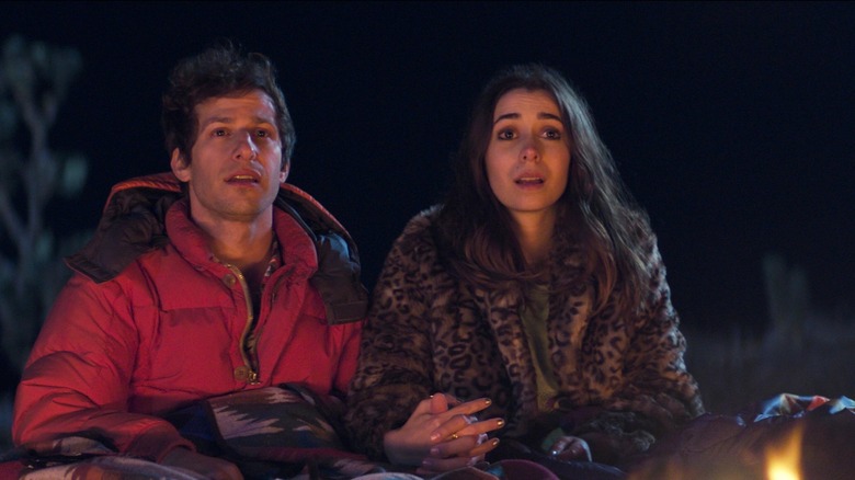 Les deux protagonistes de Palm Springs se tenant la main près d'un feu de camp (2020)