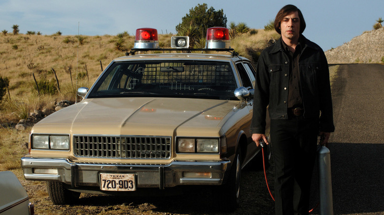 Anton Chigurh se tient à côté d'une voiture de police 