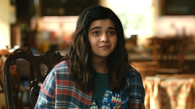 Kamala Khan souriante dans une chemise en flanelle à une table de cuisine dans Les Merveilles (2023)